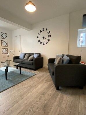 A modern living room with two sofas, a glass coffee table, and a large wall clock. - Host Stay Waterfront (Northampton)