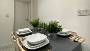 Zona pranzo con un tavolo apparecchiato per quattro persone, un orologio appeso al muro e una porta sullo sfondo.