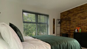 Una camera da letto moderna con un letto, una finestra con persiane, una lampada a sospensione e una parete in mattoni.