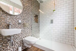 Ein Badezimmer mit Wand aus Mosaikfliesen, einem weißen Waschbecken, einer Toilette und einer Duschkabine.