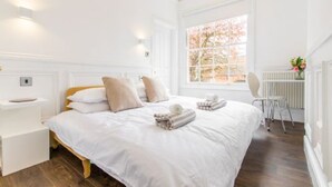 Une chambre à coucher avec un lit, des murs blancs, une fenêtre et un radiateur.