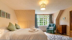 A bedroom with a bed, pillows, a chair, a window, and a lamp.