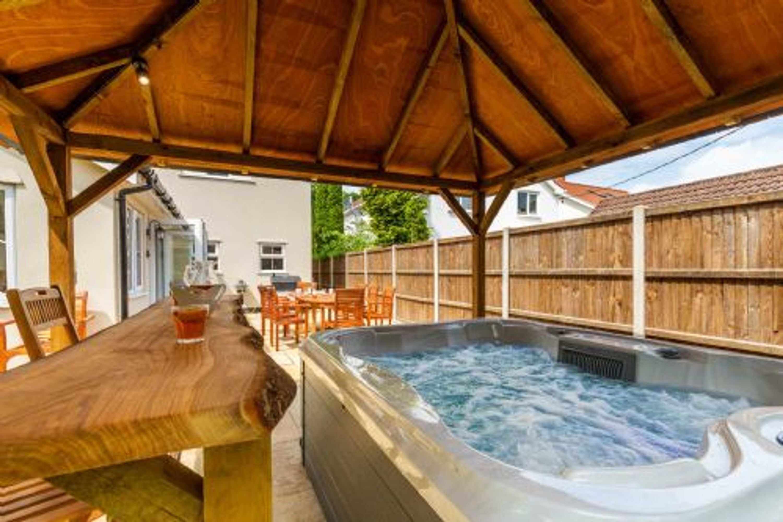 Une terrasse en bois avec un jacuzzi, une table en bois et des chaises.
