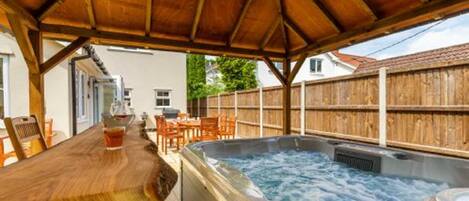 Une terrasse en bois avec un jacuzzi, une table en bois et des chaises.