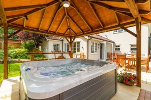 A hot tub under a wooden pergola in a backyard with a patio and outdoor furniture. - Host Stay Woodside House (Norwich)