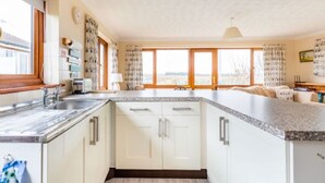 A kitchen with white cabinets, a granite countertop, and a window with curtains. - Host Stay Breezy Bungalow (North Walsham)