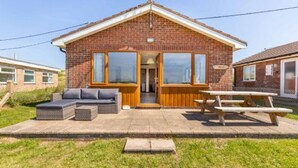 A brick house with a pitched roof, large windows, a patio with outdoor furniture, and a picnic table. - Host Stay Breezy Bungalow (North Walsham)