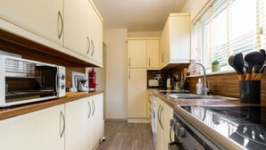 A compact kitchen with white cabinets, a microwave, a stove, and a sink. - Host Stay Corner Cottage (Norwich)