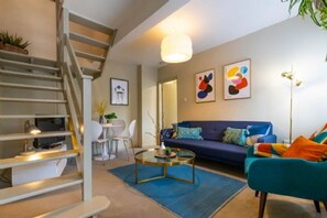 Un salon moderne avec un escalier, un canapé, une table basse et des œuvres d’art abstraites accrochées au mur.