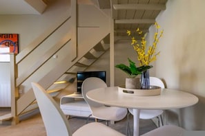 Ein modernes Interieur mit einem runden Esstisch, weißen Stühlen, einer Topfpflanze mit gelben Blüten und einer Treppe.