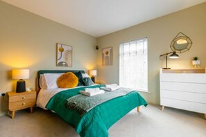 Une chambre à coucher comprenant un lit, des tables de chevet, une commode et des œuvres d’art murales.