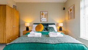 A neatly made bed with a green blanket, two bedside lamps, and a wooden wardrobe. - Host Stay Corner Cottage (Norwich)