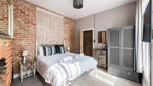 A bedroom with a brick wall, a bed with white bedding, a wardrobe, and a small bedside table with a lamp. - Host Stay Villa Otto (Cromer)