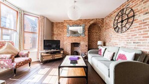 A living room with a brick fireplace, a television, a sofa, and a coffee table. - Host Stay Villa Otto (Cromer)