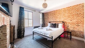 A bedroom with a brick wall, a metal bed frame, a radiator, and a hanging light fixture. - Host Stay Villa Otto (Cromer)