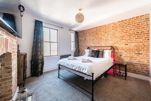 A bedroom with a brick wall, a metal bed frame, a radiator, and a hanging light fixture. - Host Stay Villa Otto (Cromer)