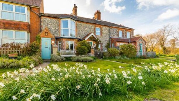 A two-story house with a stone facade, a front porch, and a garden with daffodils. - Host Stay St Joseph s Cottage (Sheringham)