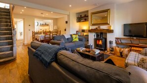 A cozy living room with a fireplace, a sofa, a television, and a staircase leading to another room. - Host Stay St Joseph s Cottage (Sheringham)