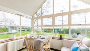 A conservatory with a table set for dining, large windows, and a view of the garden.