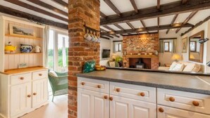 A kitchen with exposed wooden beams, a brick fireplace, and white cabinetry.