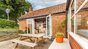 A small brick house with a tiled roof, a wooden table, and a potted plant outside.