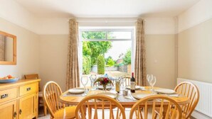 Un coin repas avec une table en bois dressée pour quatre personnes, un buffet en bois et une vue sur la verdure à l’extérieur.