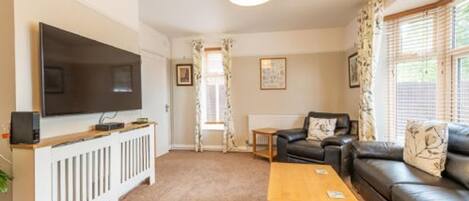 A living room with a flat-screen TV, a sofa, a coffee table, and a radiator.