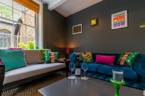 A modern living room with a sofa, a coffee table, and a window with a view of a brick building. - Host Stay Princes Cottage (Norwich)