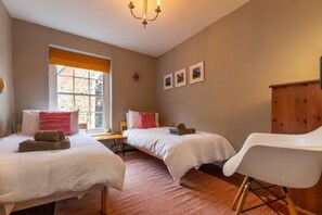 A bedroom with two beds, a wooden cabinet, and a white chair. - Host Stay Princes Cottage (Norwich)