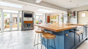 Une cuisine moderne dotée d’un grand îlot central, de tabourets de bar et offrant une vue sur l’extérieur grâce à de grandes portes coulissantes.