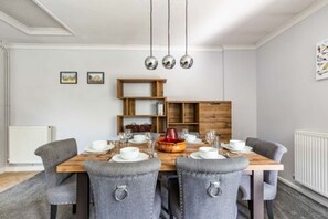 A dining area with a wooden table set for four, grey upholstered chairs, and a wooden bookshelf in the background. - Host Stay Church Close (Norwich)