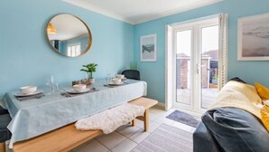 A room with a bed, a dining table set with plates, glasses, and a bowl, a round mirror on the wall, and a view through a glass door. - Host Stay Gorse Cottage (Norwich)