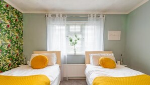 Un dormitorio con dos camas, una ventana con cortinas blancas y una pared decorada con un estampado de motivos tropicales.