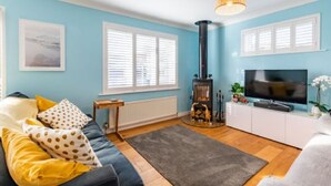 A living room with a sofa, a television, a fireplace, and a window with blinds. - Host Stay Gorse Cottage (Norwich)
