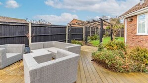 Un patio con mobiliario de mimbre, una terraza de madera y una casa de ladrillo al fondo.