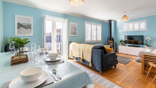 A modern living room with a sofa, a dining table set for two, and a television. - Host Stay Gorse Cottage (Norwich)