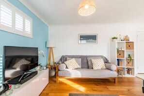 A living room with a sofa, TV, and wooden flooring. - Host Stay Gorse Cottage (Norwich)