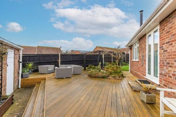A wooden deck with outdoor furniture, a brick house, and a fenced backyard. - Host Stay Gorse Cottage (Norwich)