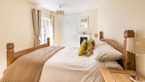 A bedroom with a wooden bed, a bedside table, a lamp, and a window with curtains. - Host Stay West Street Cottage (Cromer)