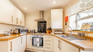 A modern kitchen with white cabinetry, a built-in oven, microwave, and a stainless steel range hood. - Host Stay West Street Cottage (Cromer)