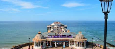 A seaside promenade with a central building featuring a dome structure, a pier extending into the sea, and a lamp post.