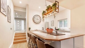 A modern kitchen with a central island, bar stools, a clock, and a hanging plant. - Host Stay Crimond House (Cromer)