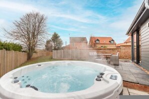 A hot tub in a backyard with a wooden fence, a brick house, and a patio table. - Host Stay Crimond House (Cromer)