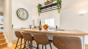 A modern kitchen with a central island, bar stools, and a clock on the wall. - Host Stay Crimond House (Cromer)