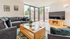 A modern living room with a grey sofa, a wooden coffee table, and a flat-screen TV. - Host Stay Crimond House (Cromer)