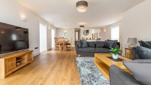 A modern living room with a large flat-screen TV, wooden flooring, a dark grey sofa, and a coffee table. - Host Stay Crimond House (Cromer)