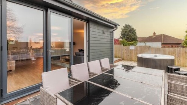 A patio with a glass table and chairs, a hot tub, and a sliding glass door leading to an indoor area. - Host Stay Crimond House (Cromer)