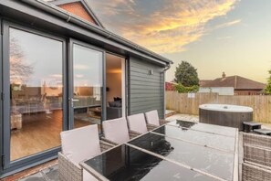 Eine Terrasse mit Glastisch und -stühlen, einem Whirlpool und einer Glasschiebetür zu einem Innenbereich.