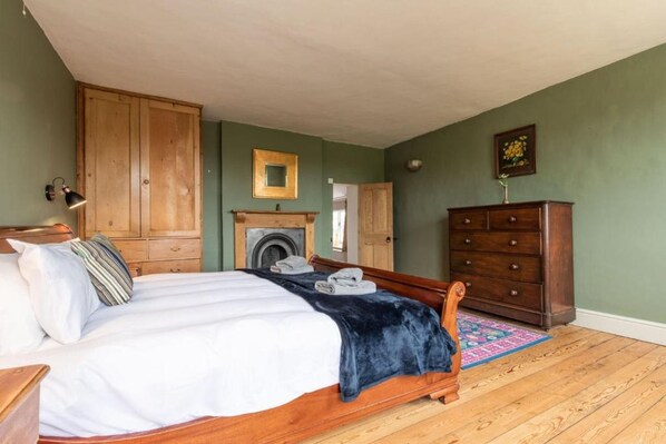 A bedroom with a wooden bed, a dresser, a wardrobe, a fireplace, and a rug.