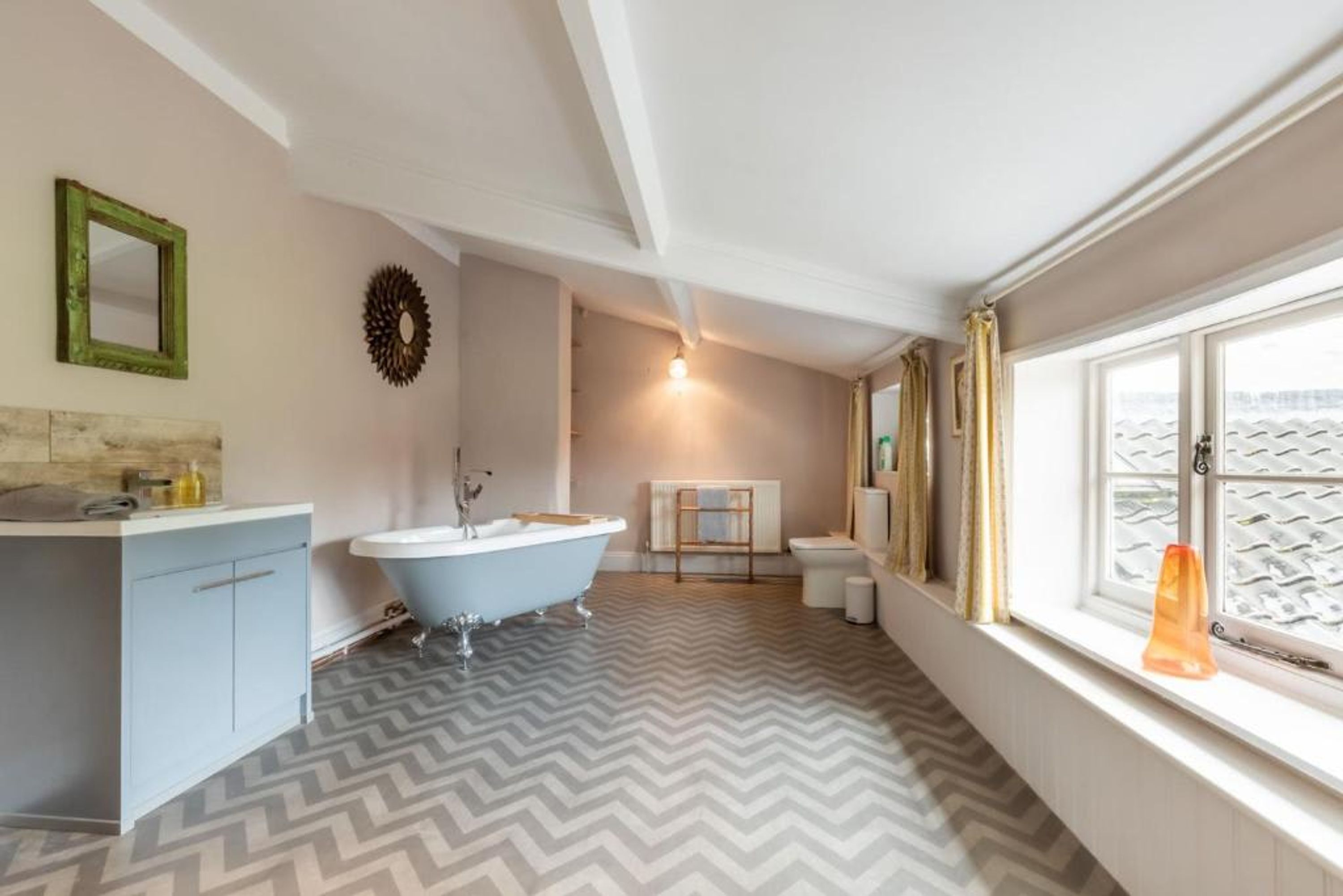 A bathroom with a freestanding bathtub, a vanity with a mirror, a radiator, and a window with curtains.